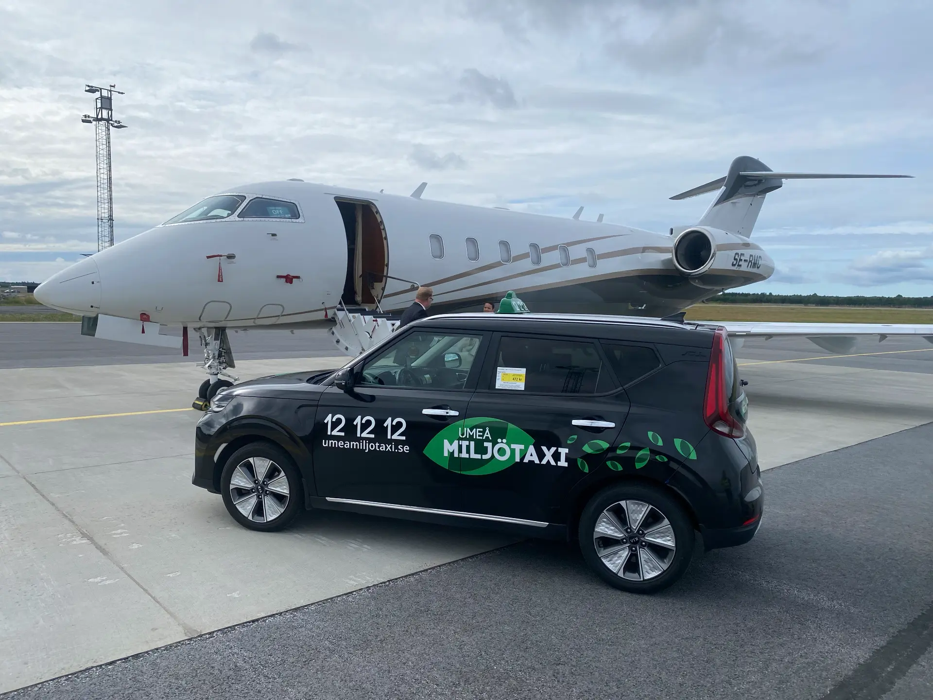 Umeå Miljötaxis bil framför ett privatplan på Umeå Airport